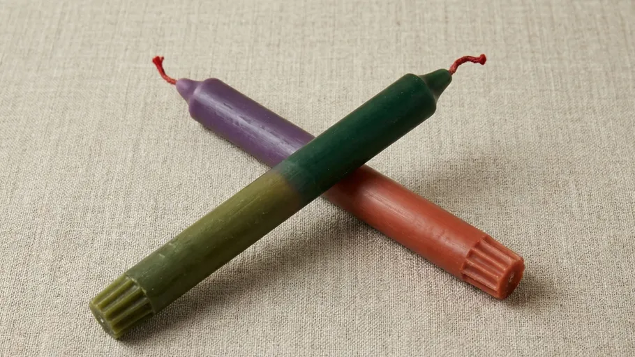 Two colored candles crossed on a fabric surface.