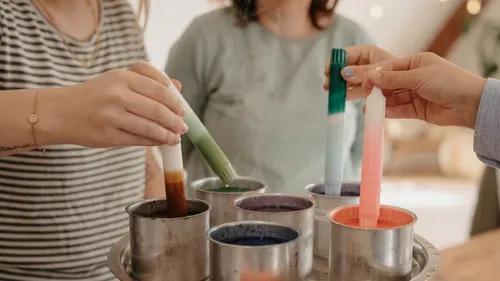 Hände tauchen Kerzen in bunte Wachstöpfe.