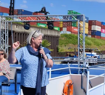 Frau spricht auf Boot, Container im Hintergrund.