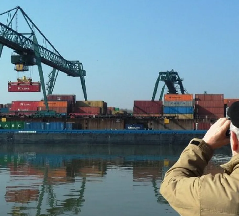 Person fotografiert Kräne beim Laden von Containern.