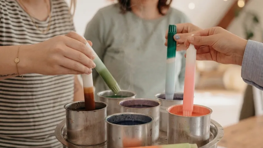 Hands dipping candles into colorful wax.