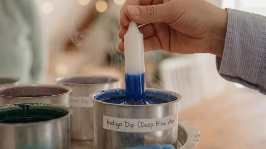 Hand dipping candle into blue wax.