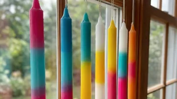 Bunte Kerzen hängen nahe einem Fenster.
