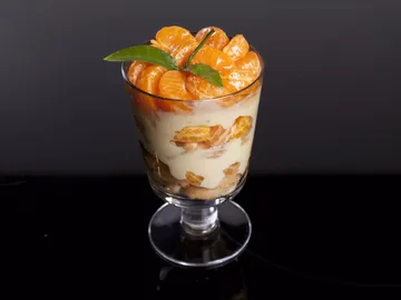 A glass of dessert with tangerines, cream and cookies.