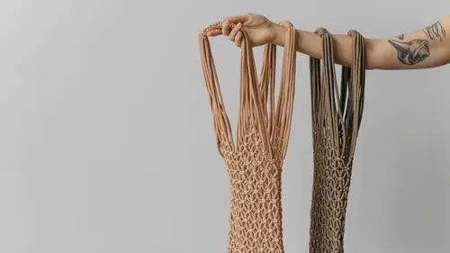 Hand hält zwei gehäkelte Taschen vor grauem Hintergrund.