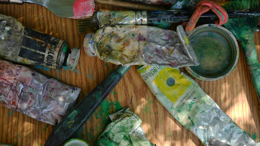 Messy paint tubes and brushes on wooden table.