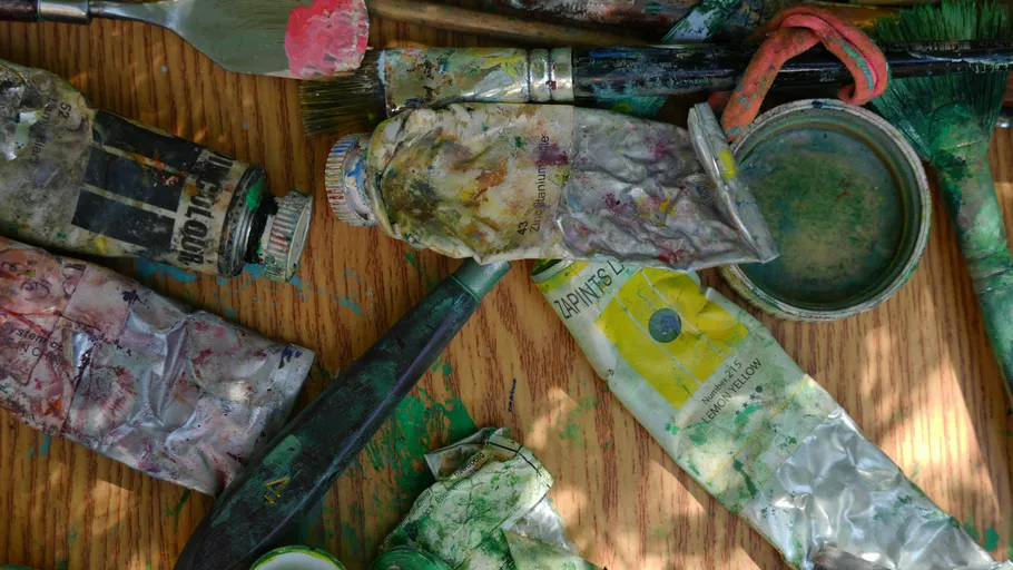 Paint tubes and brushes on wooden table.