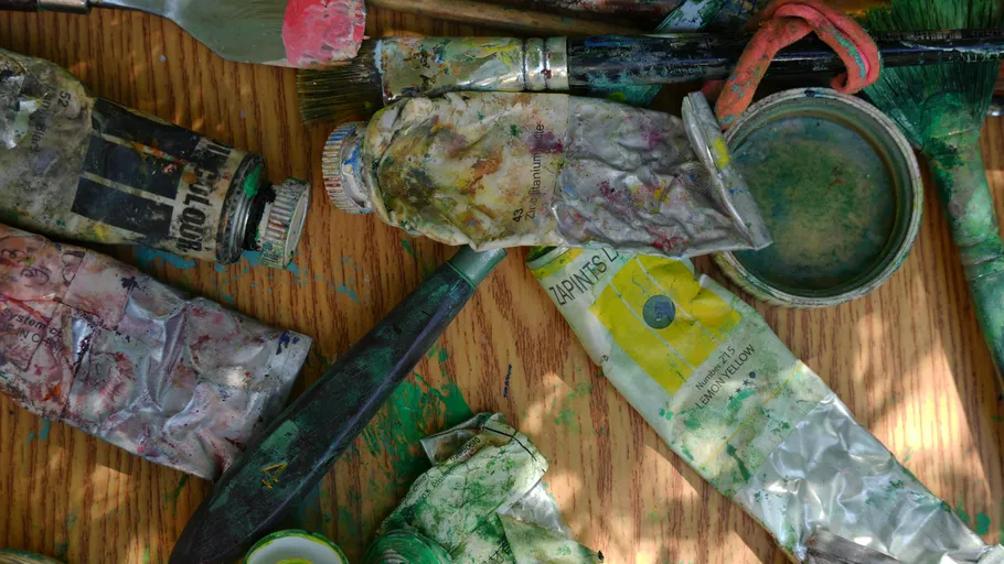 Paint tubes and brushes on wooden surface.