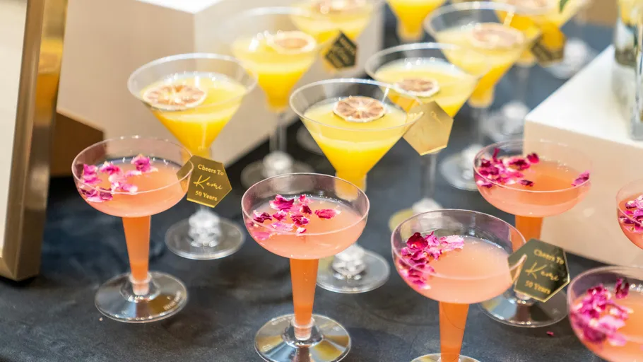 Bunte Cocktails mit Blumen auf schwarzem Tisch.