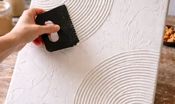 Hand ritzt Textur auf Gipsleinwand.
