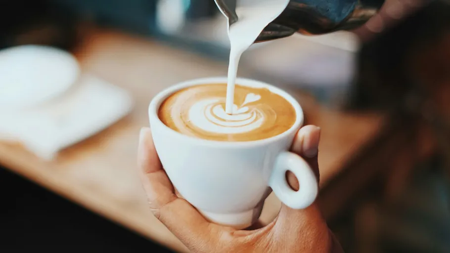 Hand gießt Milch in eine Cappuccino-Tasse.