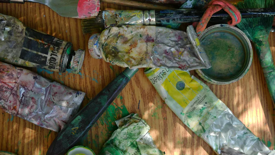 Paint tubes and brushes on wooden table.