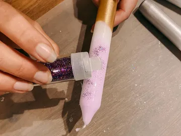A hand sprinkles glitter on a pink candle.