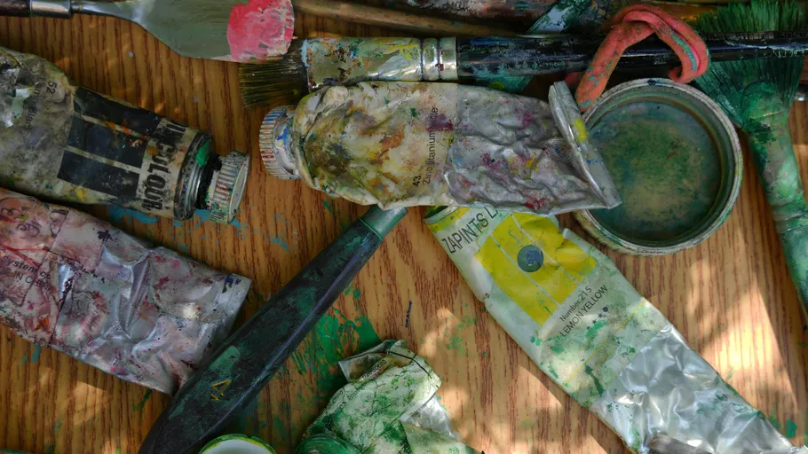 Paint tubes and brushes on wooden table.