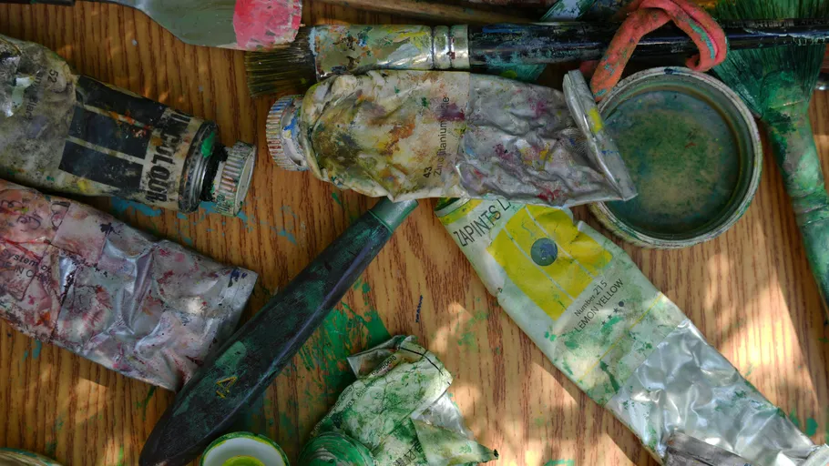 Verwendete Farbtuben und Pinsel auf Holzoberfläche.