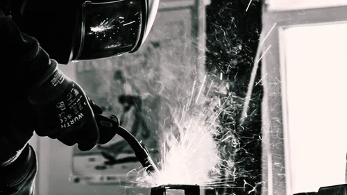 Welder creating sparks indoors, wearing helmet.