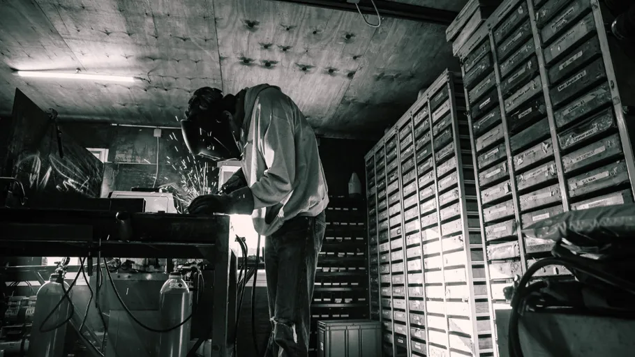 Person welding in a dimly lit workshop.