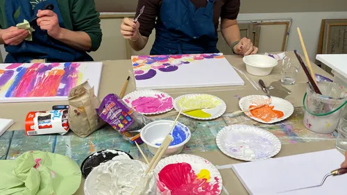 Artists painting colorful canvases at a table.