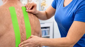 Person applying green tape to man's back.
