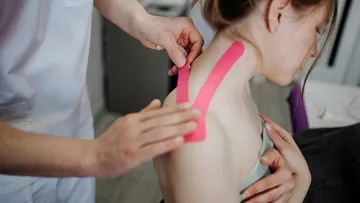 Person klebt pinkes Tape auf Frauenschulter.