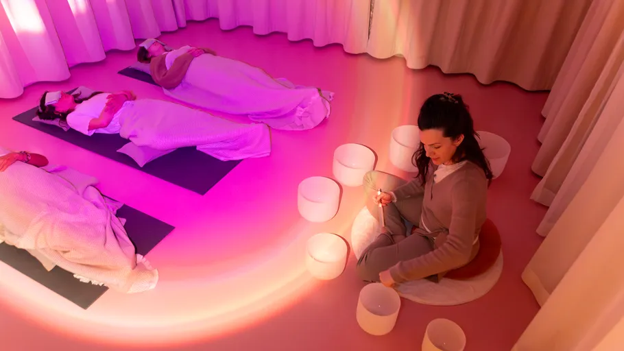 Woman playing bowls with others meditating nearby.