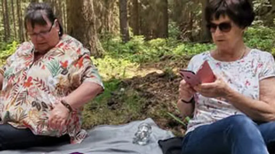 Two women sitting on a blanket in a forest.