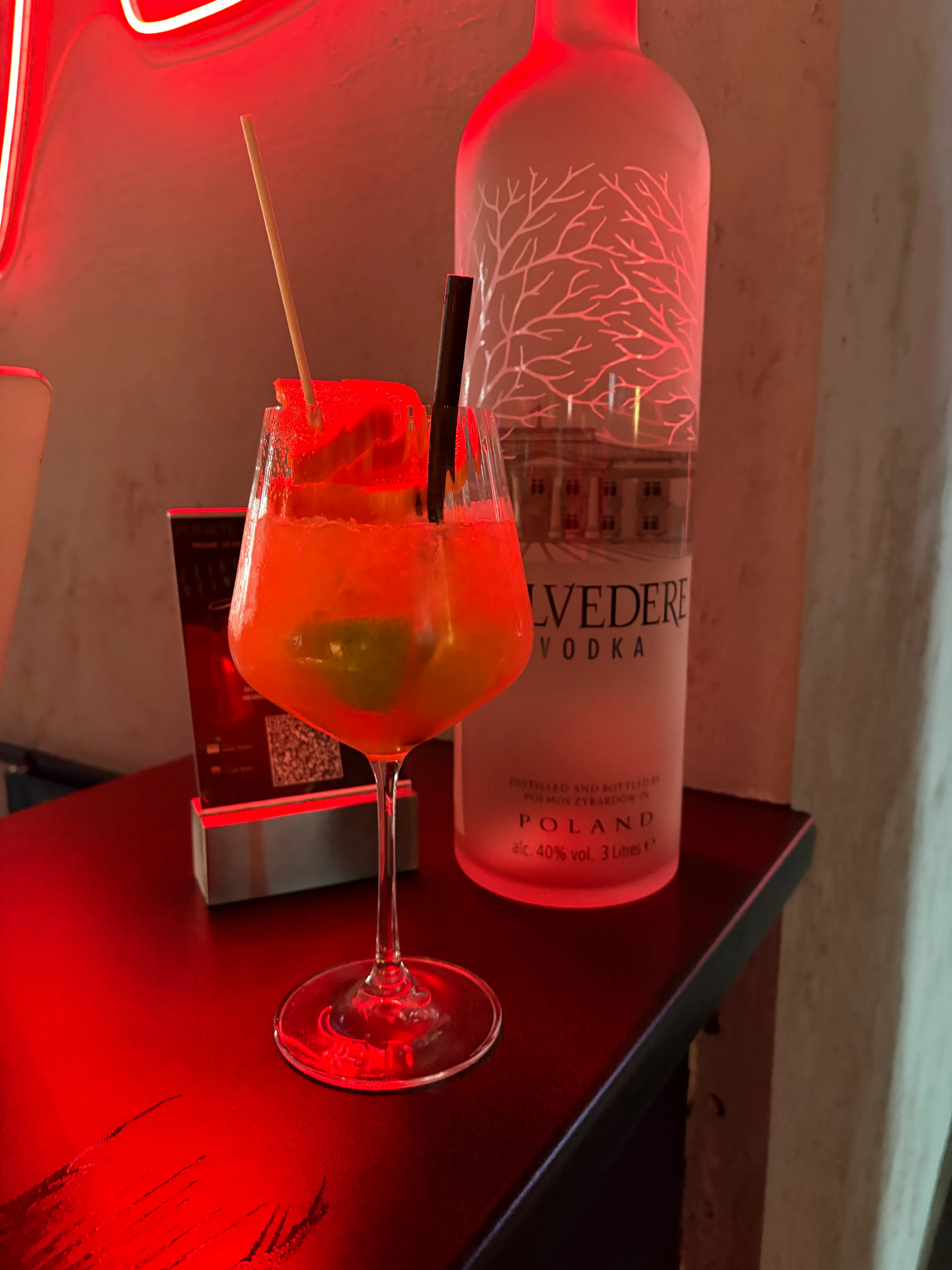 Cocktail mit Früchten neben großer Wodkaflasche.
