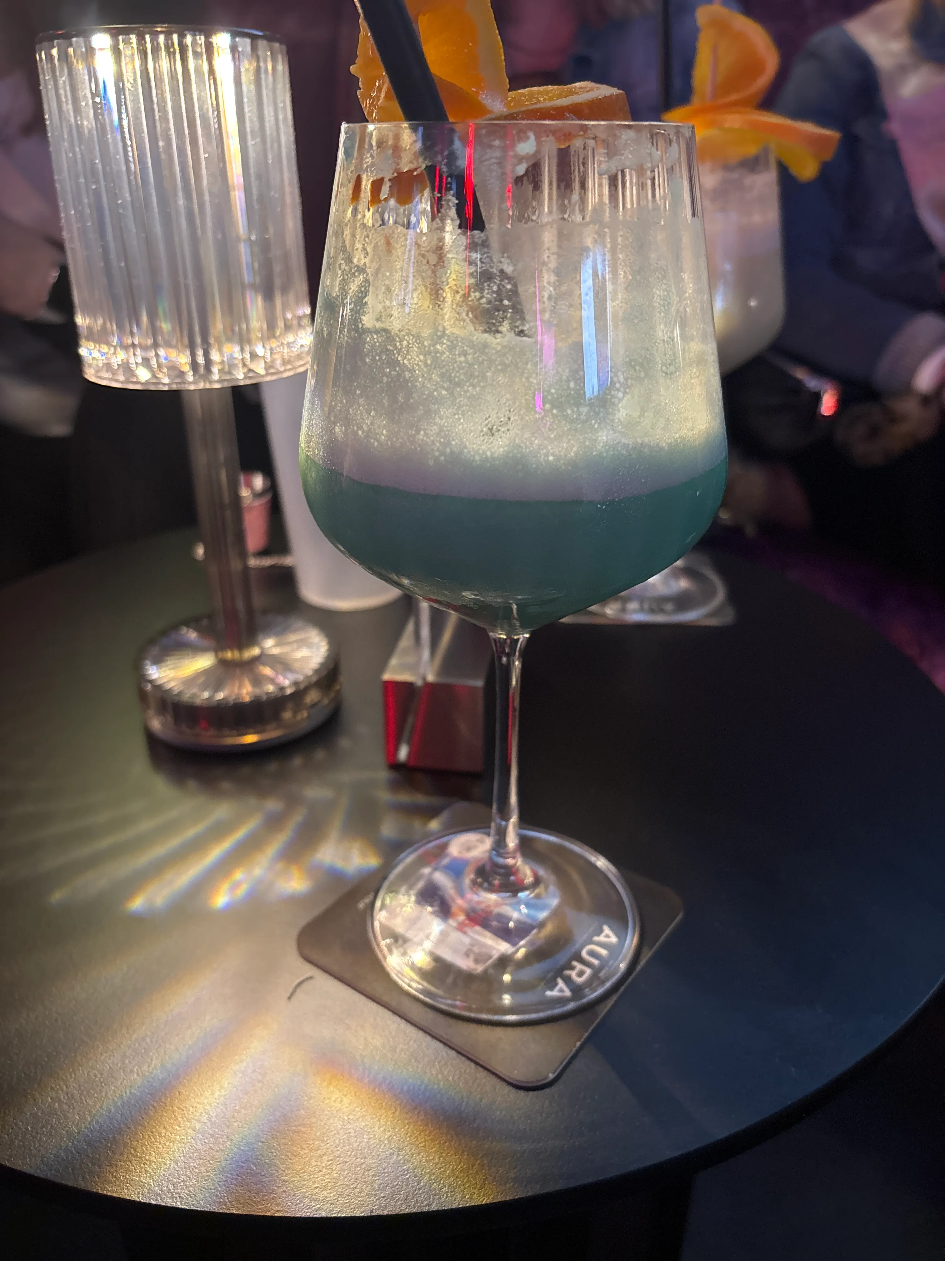 Blauer Cocktail mit Orangenscheiben auf Tisch.