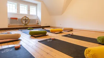 Yoga mats with bolsters in a wooden-floored studio.