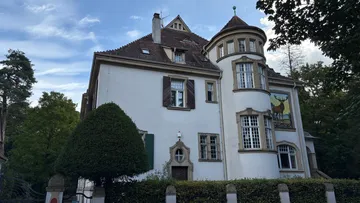 Large house with a round turret, trees surrounding.