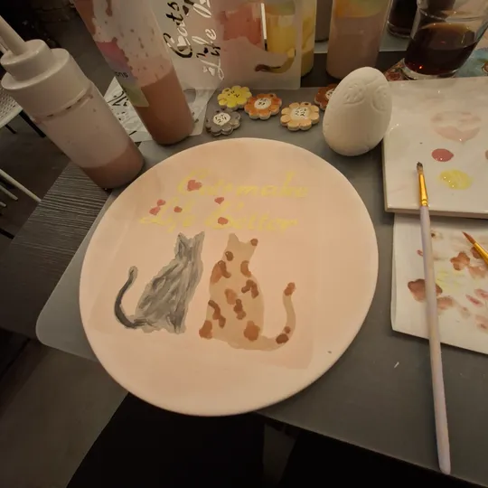 Hand-painted plate with two cats, art supplies nearby.