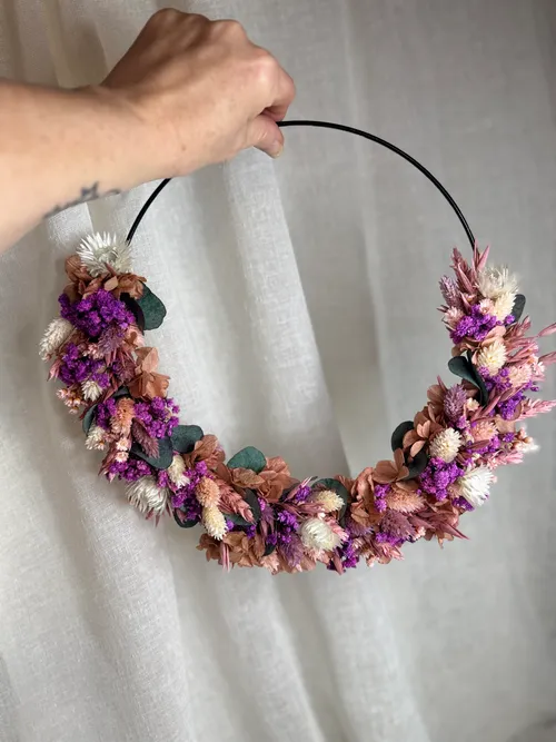 Hand holding floral wreath against curtain.