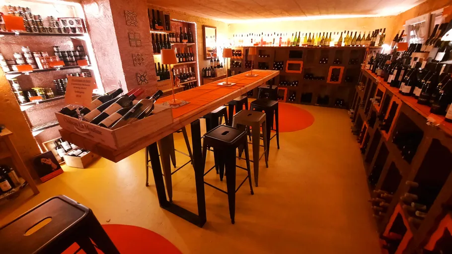 Wine cellar with bottles and stools, warm lighting.