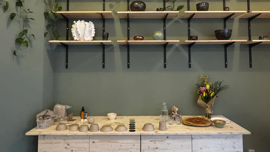 Wooden shelves with pottery on green wall.