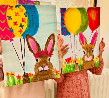 Children holding colorful bunny paintings with balloons.