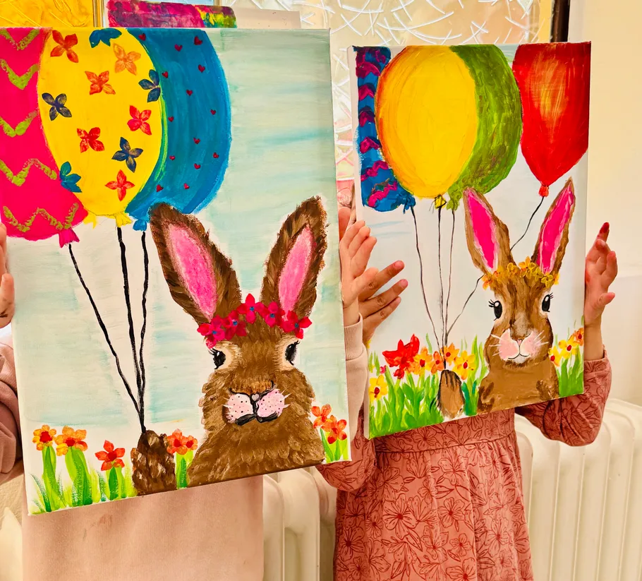 Kinder halten bunte Hasengemälde mit Luftballons.