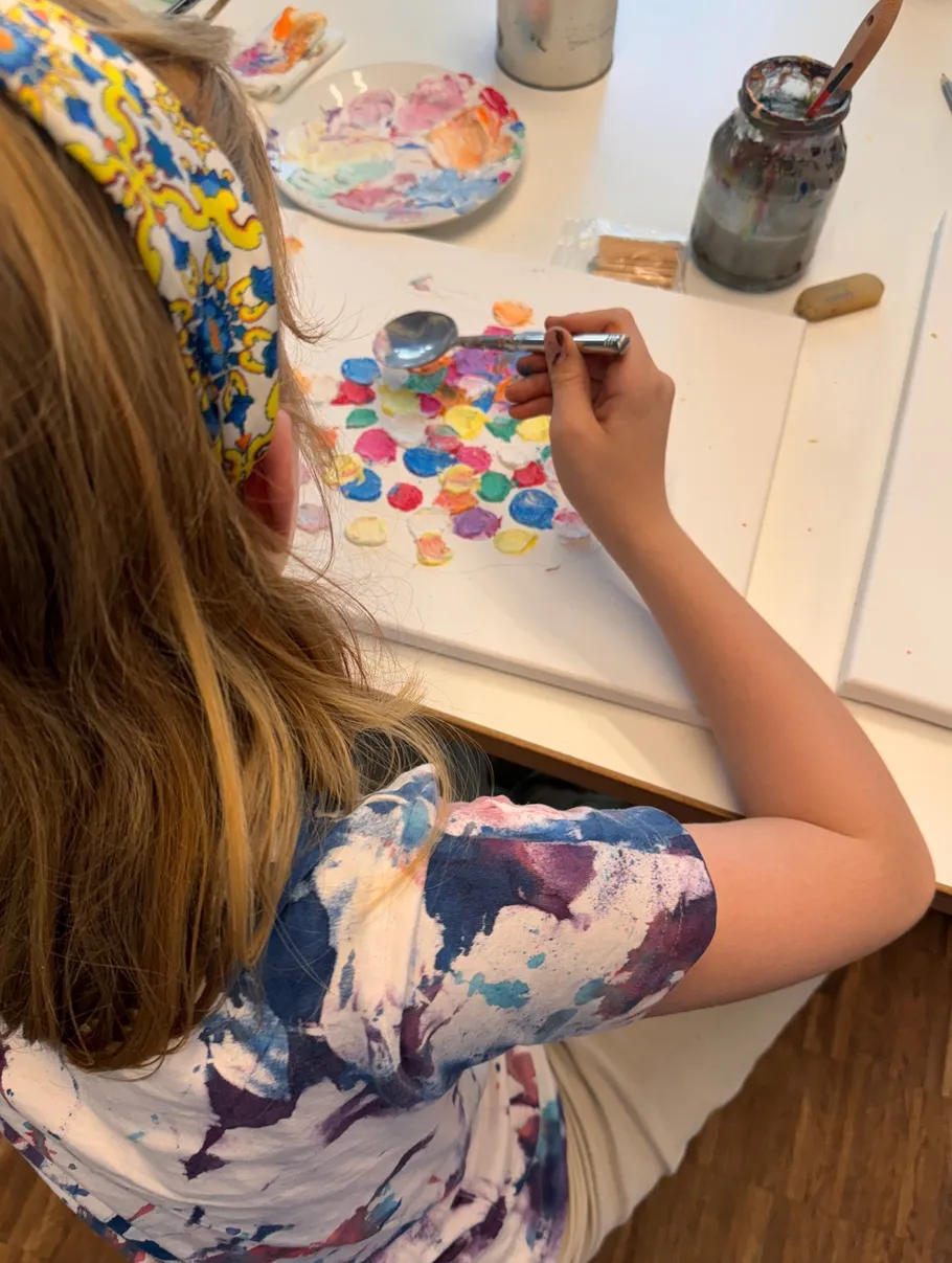 Child painting colorful circles on canvas at table.
