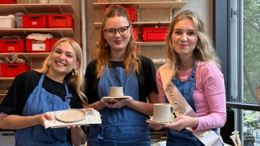 Three women in aprons holding pottery objects.