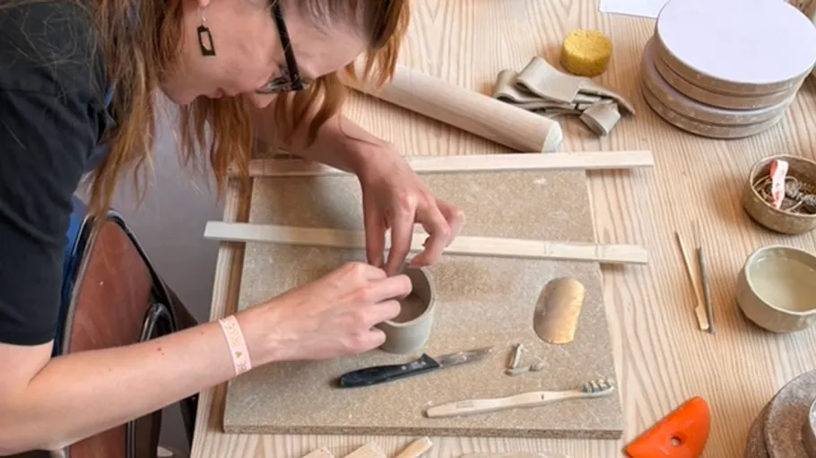 Woman crafting pottery at wooden table.