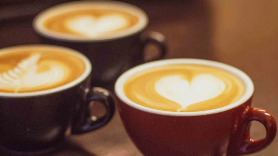 Drei Cappuccinos mit Latte Art auf Tisch.