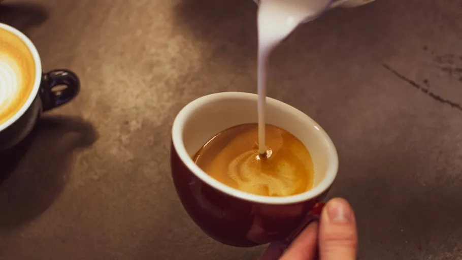 Hand gießt Milch in Espressotasse.