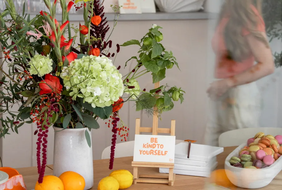 Flower vase, card, and fruits on table.
