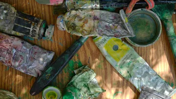 Used paint tubes and brushes on wooden table.