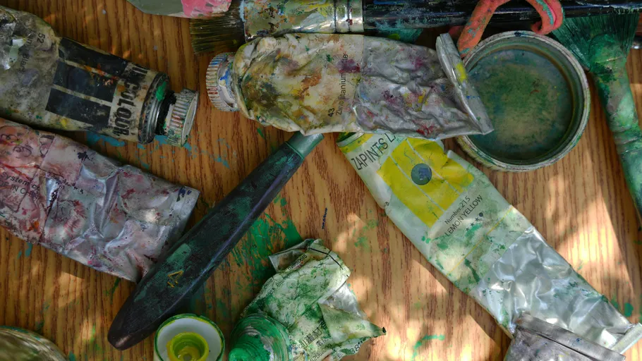 Verbrauchte Farbtuben und Pinsel auf Holztisch.