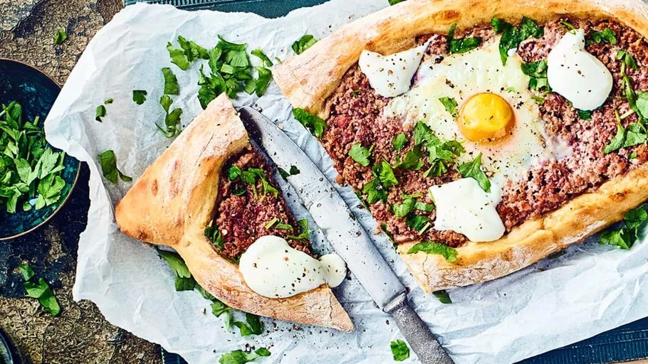 Bread boat with meat, egg, herbs on paper.