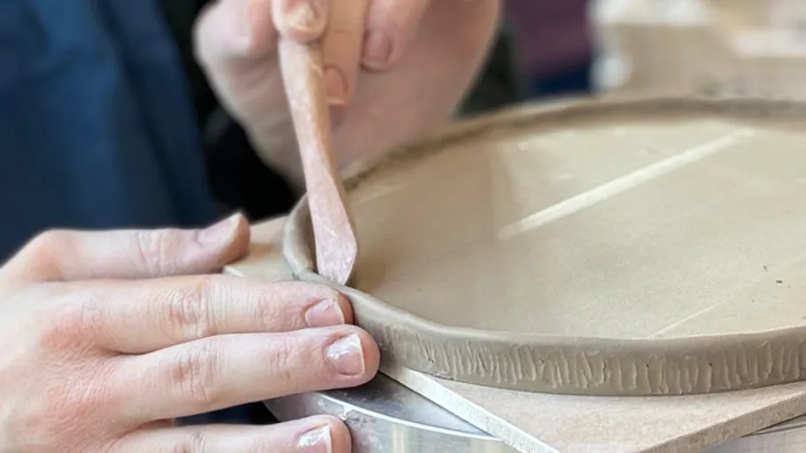 Hands shaping clay plate on pottery wheel.
