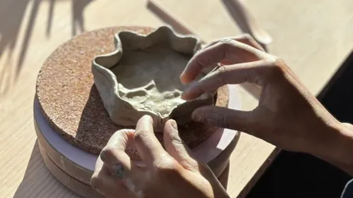 Hands shaping clay bowl on a wooden table.