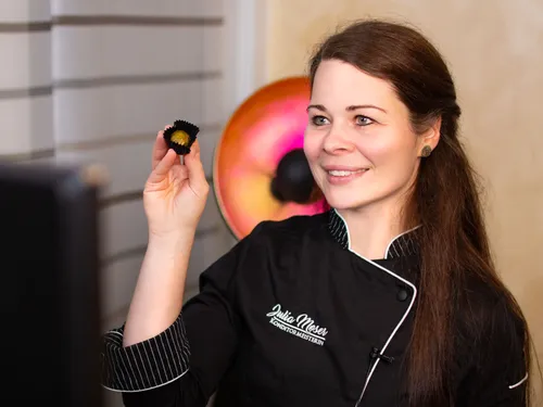 Pastry chef holds chocolate and smiles in front of a computer screen.