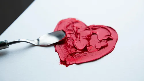 Malmesser verteilt rote Farbe in Herzform.