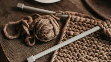 Knitting needles with brown yarn on table.